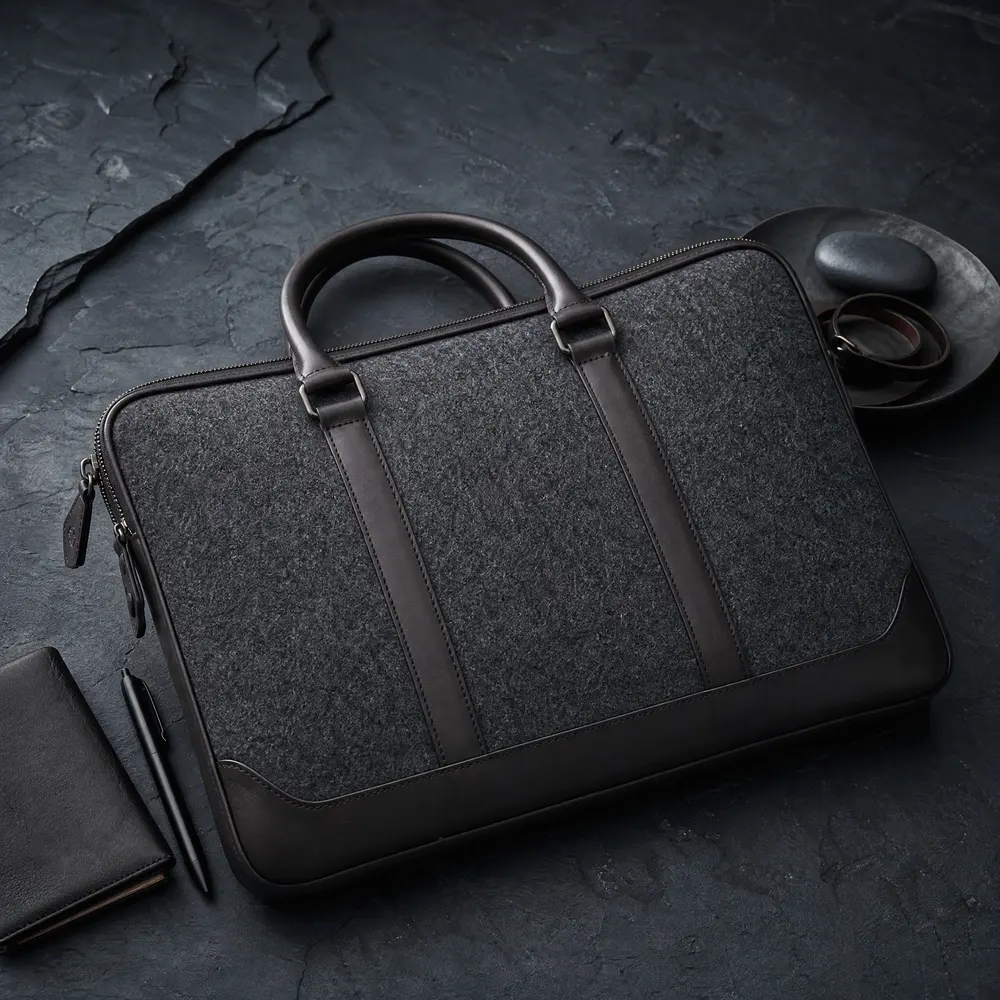 Anthrazitfarbene Laptoptasche aus Wollfilz mit dunklen Lederbesätzen und Griffen auf Schiefer
